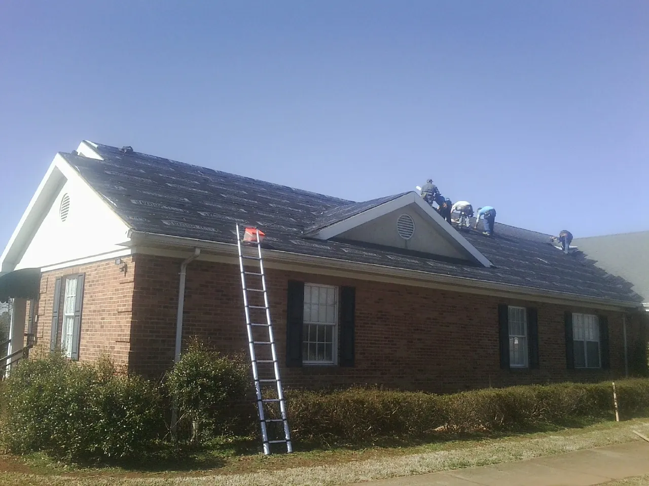 Crew tearing shingles off a brick ranch roof with a ladder set — Metal Roof Repair work by our crew in Bethel